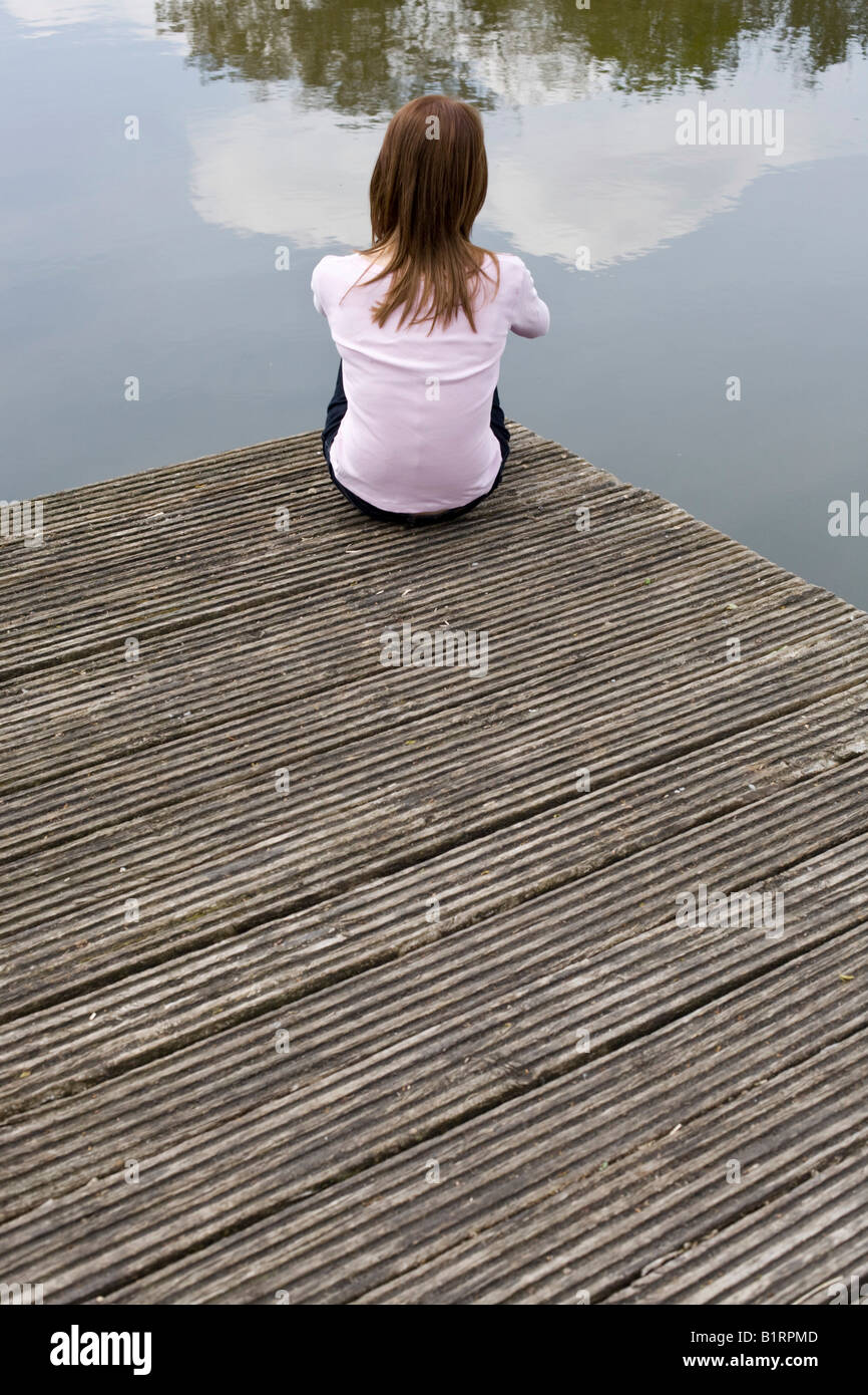 Young woman sitting on a jetty, wooden dock, looking at the water Stock Photo