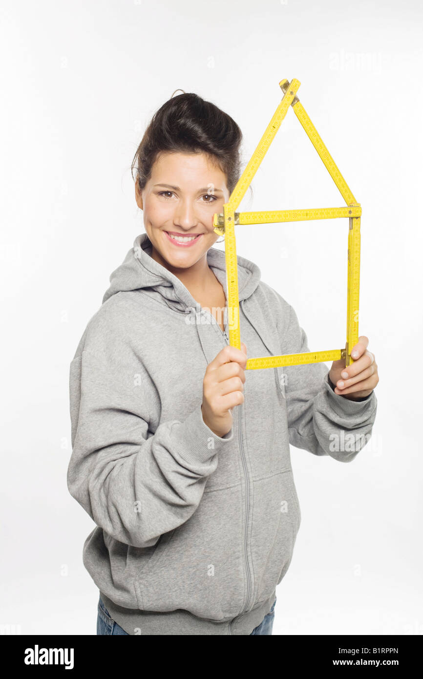 Young woman smiling into the camera holding in her hands a yellow folding ruler folded in the shape of a house Stock Photo