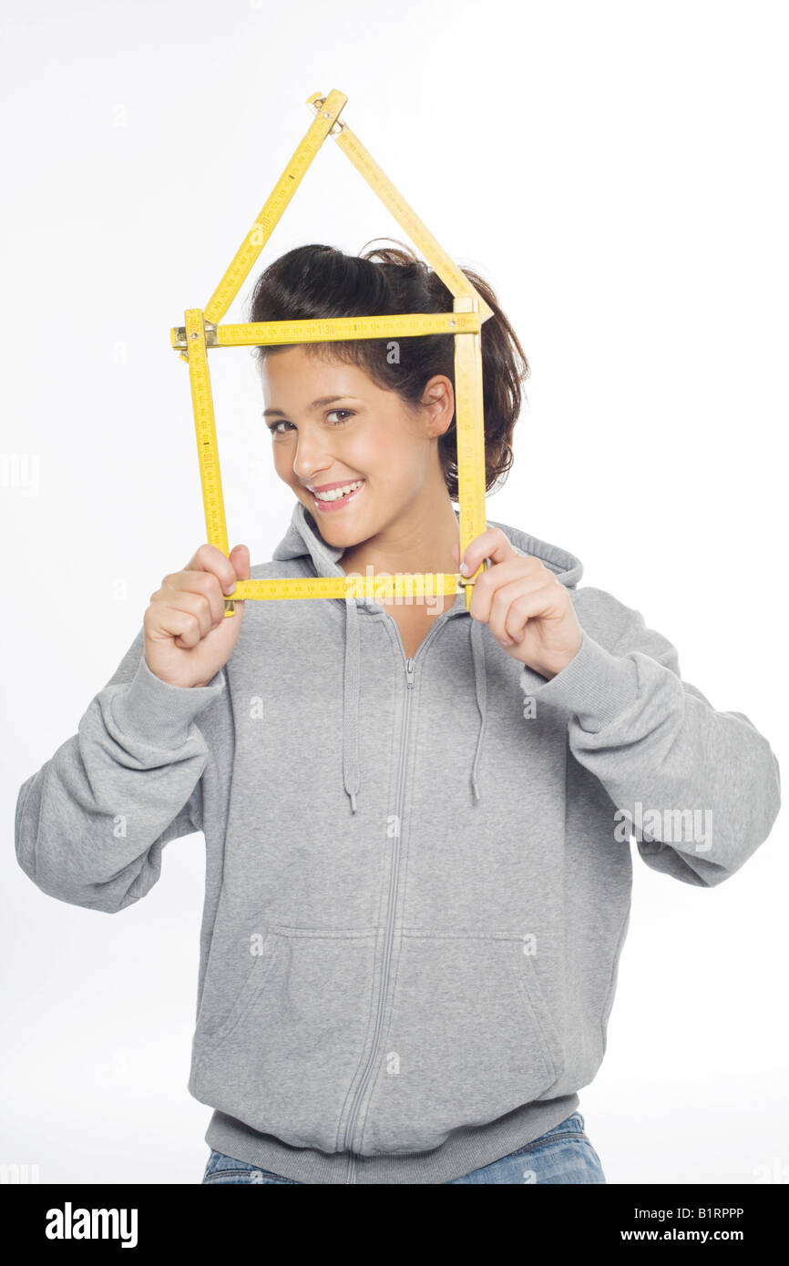 Young woman smiling into the camera holding in her hands a yellow folding ruler folded in the shape of a house Stock Photo