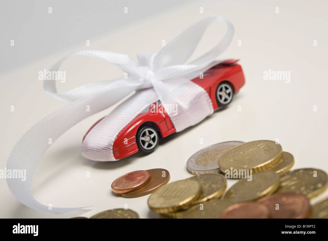 Euro coins, red toy car, wrapped with a white bow as a present Stock Photo