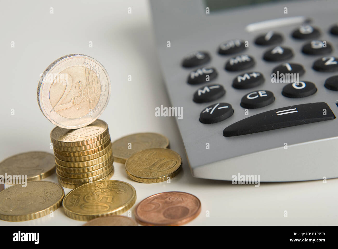 Stacked Euro coins next to a calculator Stock Photo