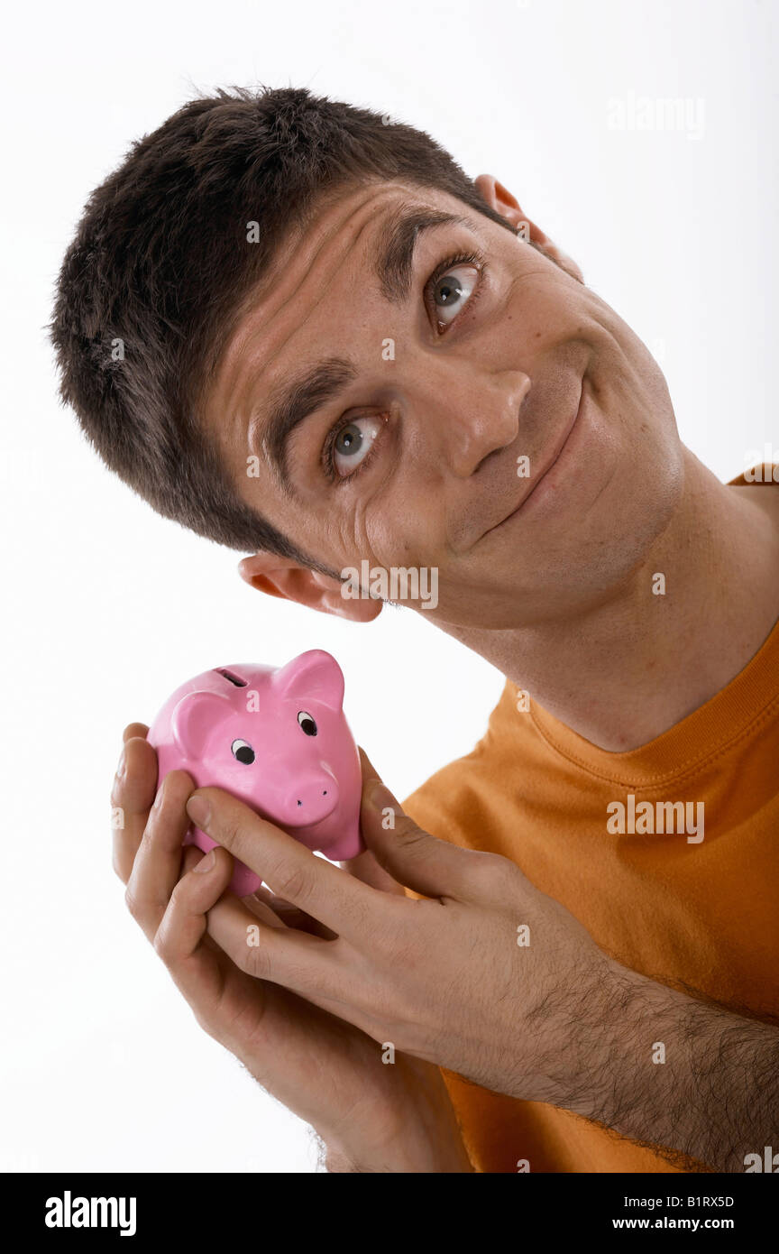 Smiling man holding a piggybank up to his ear Stock Photo - Alamy