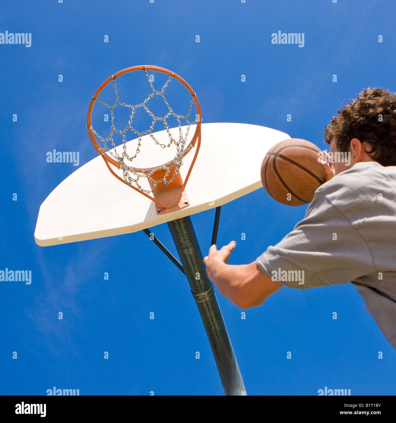 A teen basketball player jumps to shoot at the basket Stock Photo