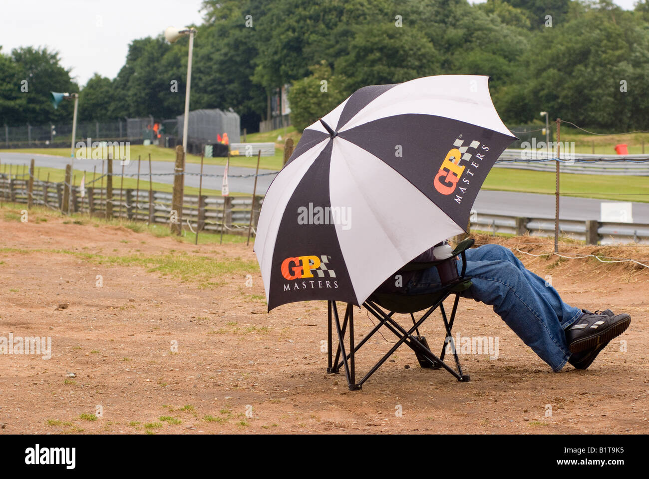 Spectator Overlooking the Avenue Sitting Under Umbrella at Oulton Park Motor Racing Circuit Cheshire England United Kingdom UK Stock Photo