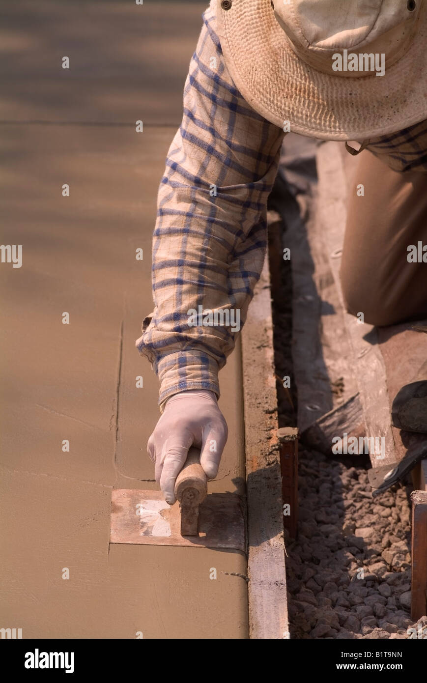 Workman uses a trowel to finish a new concrete driveway in front of a