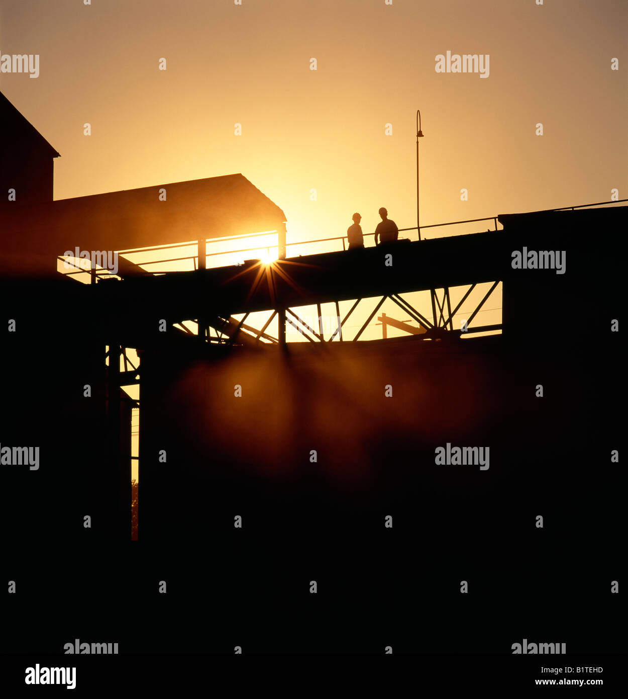 Workers silhouetted against the sunrise at a cement plant. Stock Photo