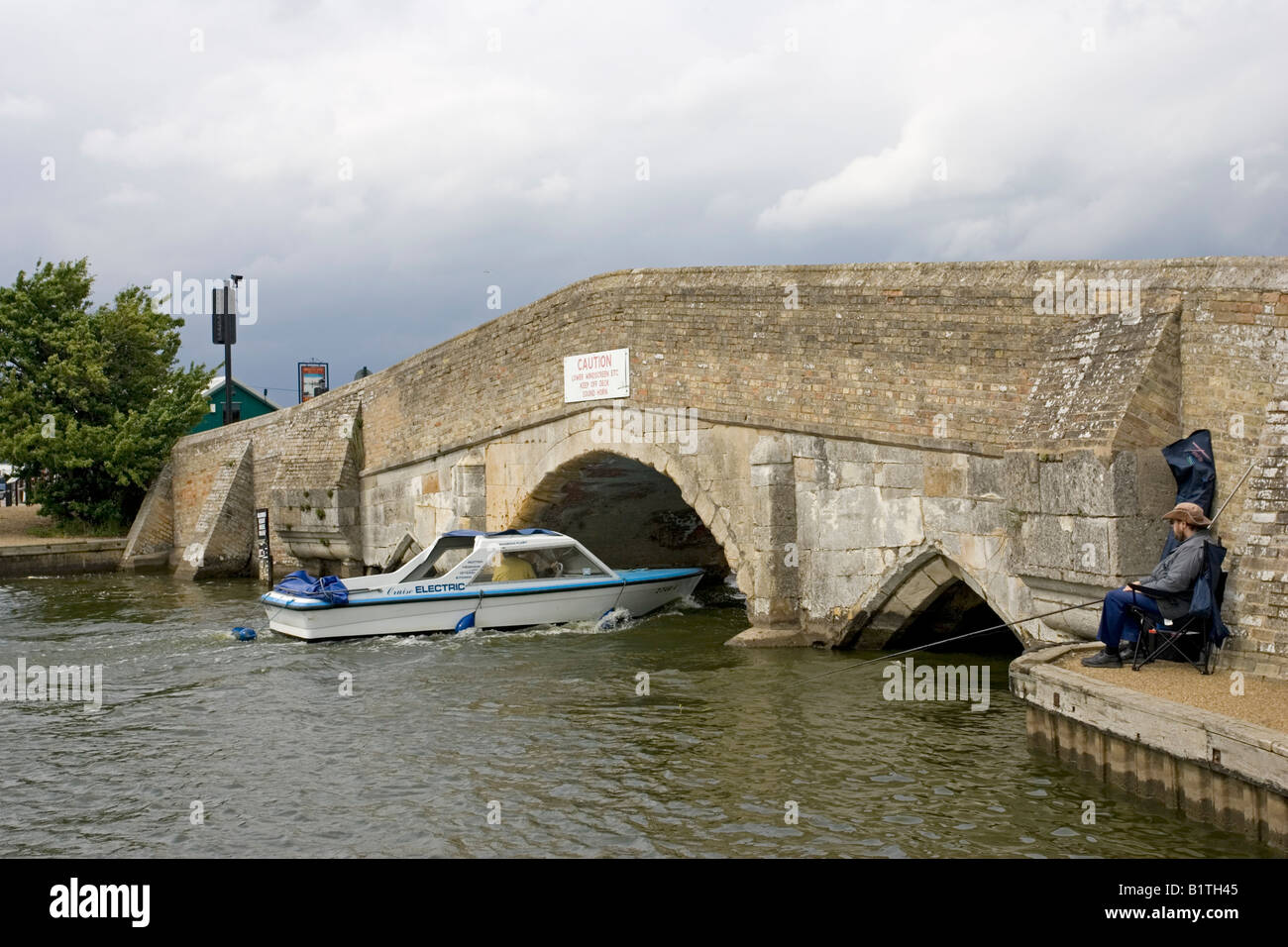 Electric boat passing through low arch Potter Heigham stone bridge