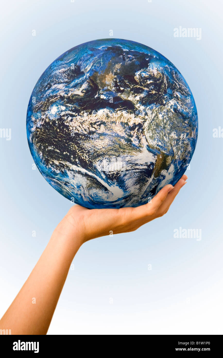 Planet earth is seen gently cupped in the palm of someone's hand, against a plain blue background. Stock Photo