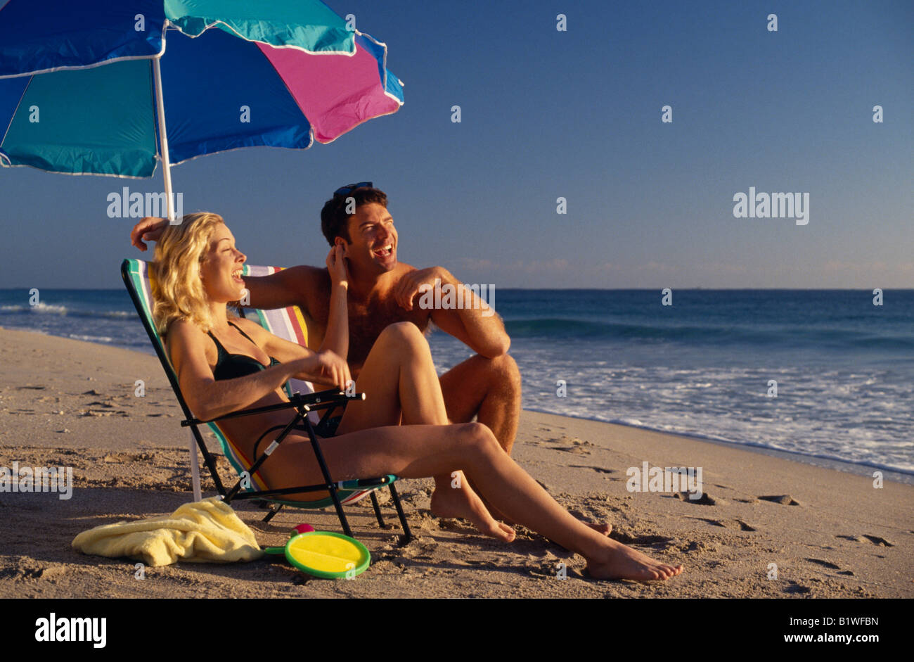 USA North America Florida Fort Lauderdale Young couple on sandy beach sitting under a parasol umbrella Stock Photo