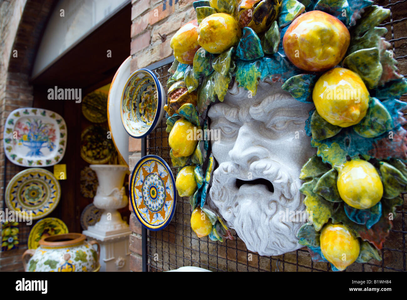 ITALY Tuscany San Gimignano Ceramics shop display of colourful plates and face of bearded man with fruit and vines in his hair Stock Photo