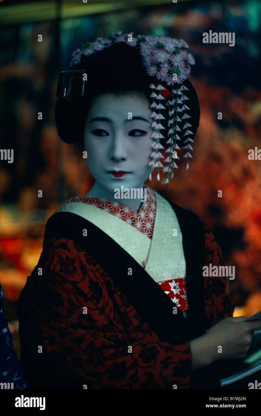 JAPAN Kyoto Gion maiko or apprentice geisha with white powdered face and red painted lips wearing richly patterned kimono Stock Photo