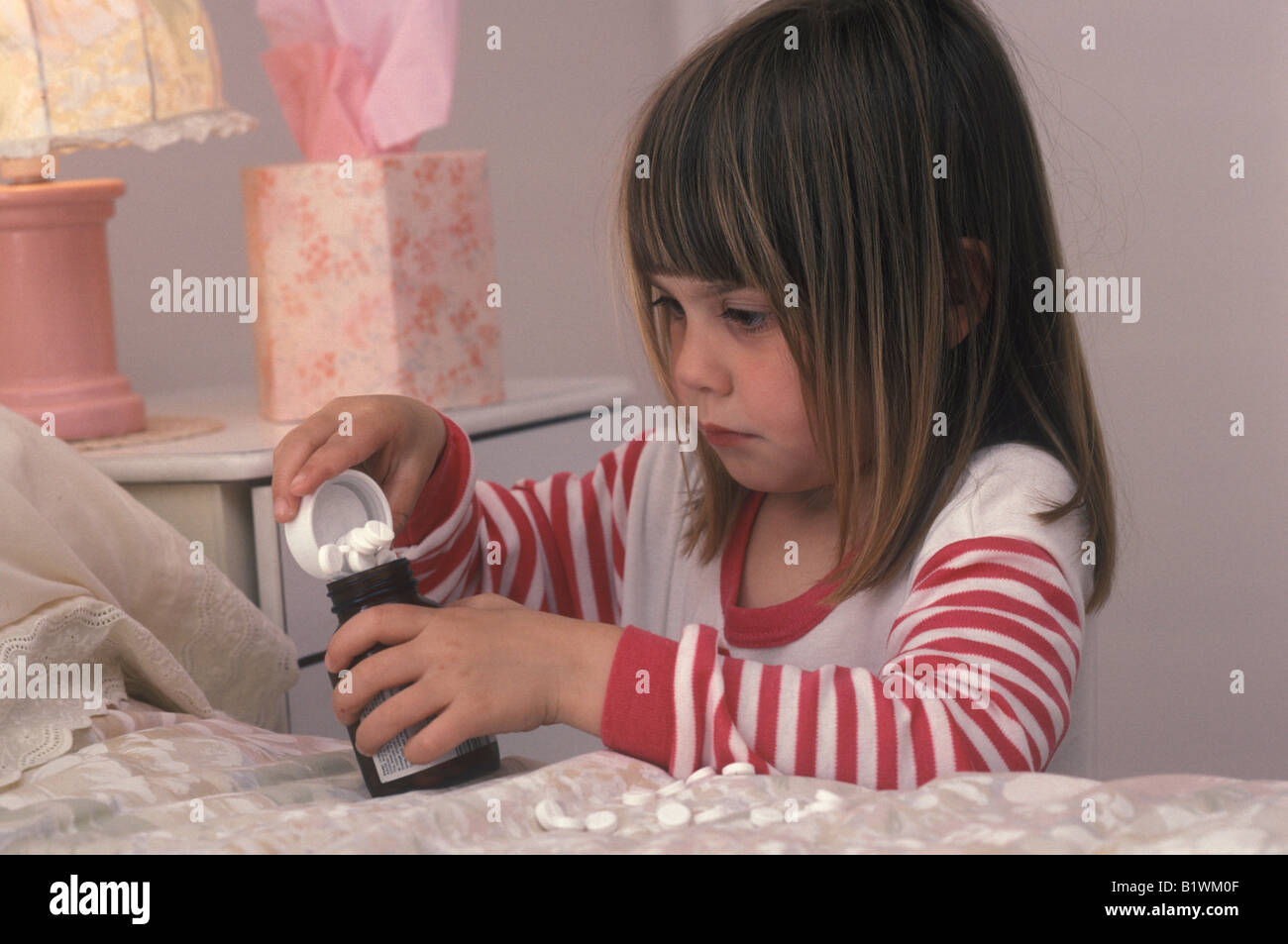 Young girl looking at pills from a bottle on the bed Stock Photo