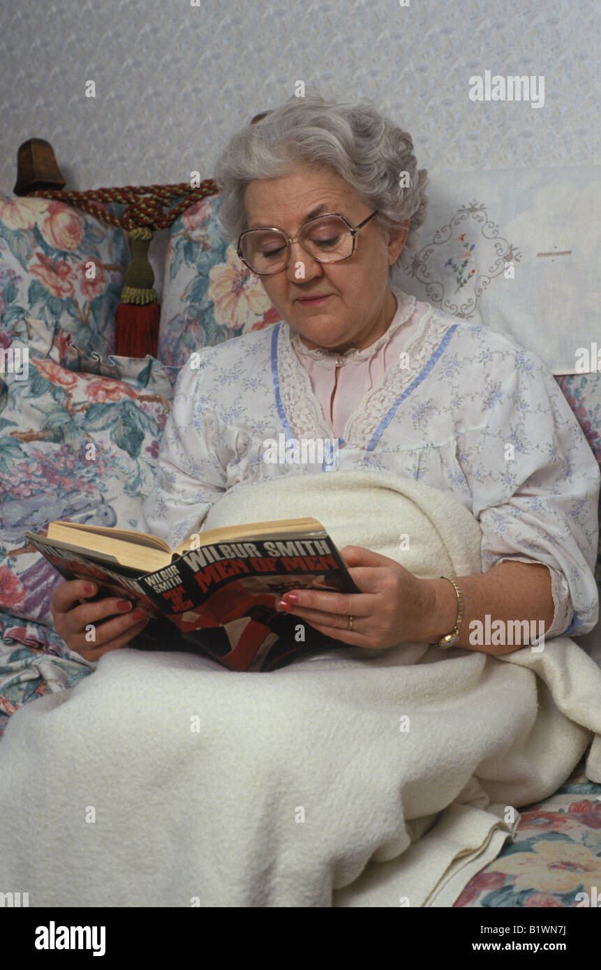 elderly woman in bed reading a book Stock Photo