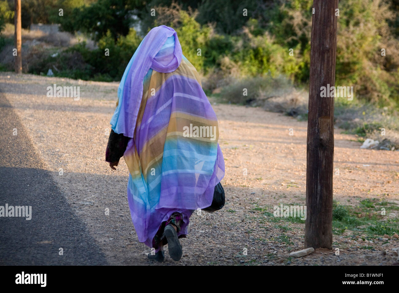 Woman wearing headcover shawl walking along road. Morocco. North West Africa. Horizontal. 89316 Morocco Stock Photo