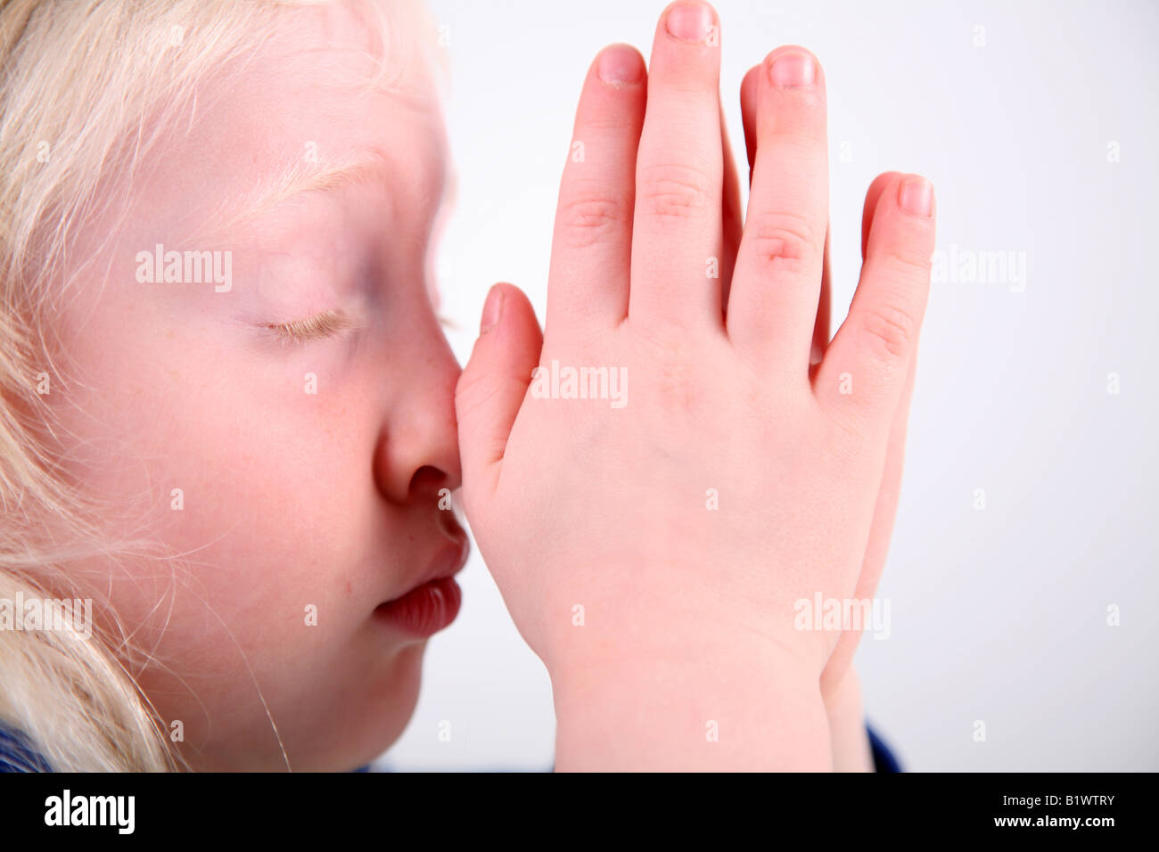 Close up shot of a blonde haired little girl saying her prayers, against a white background. Stock Photo