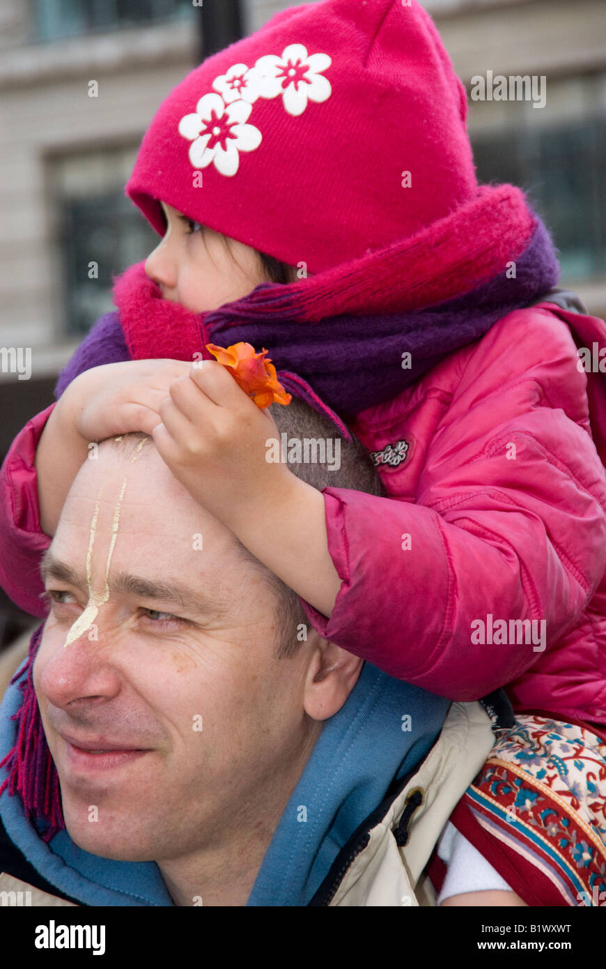 Hare Krishna devotee with child on shoulder holding blossom in Leicester Square Guara Purnima ceremony of Lord Caitanya Stock Photo