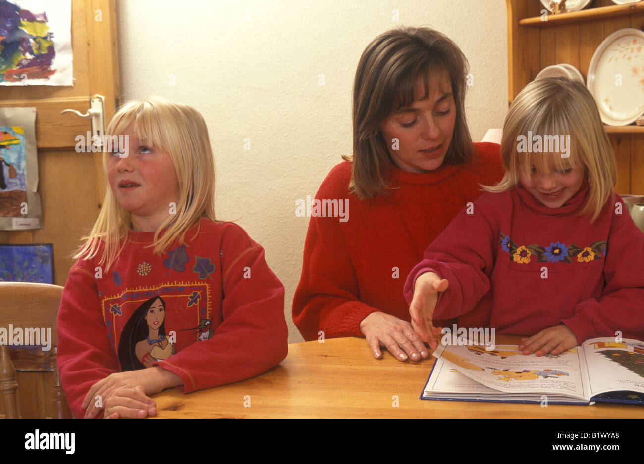 mother reading to daughter with another child looking bored Stock Photo