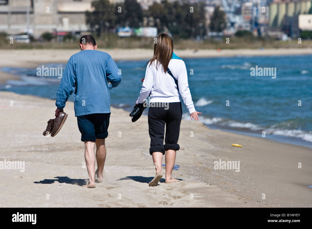 Couple walk barefoot along beach in Catania, Sicily, Italy Stock Photo