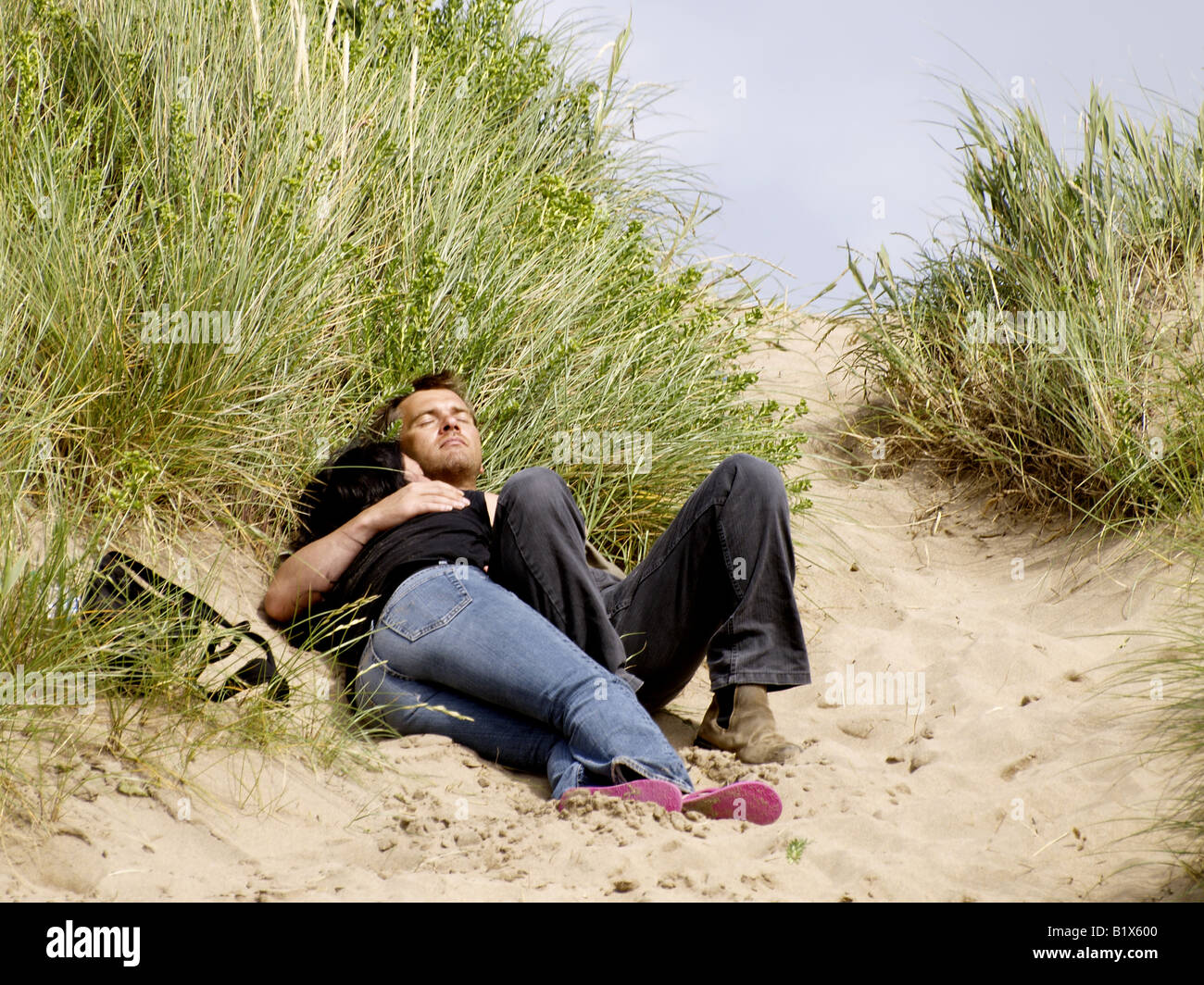 Couple cuddled in the sand dunes on a beach Stock Photo