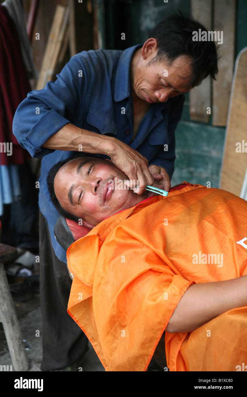Man gets a shave outside the the remains of the barber's in earthquake affected Cifeng, Pengzhou, Sichuan Province, China Stock Photo