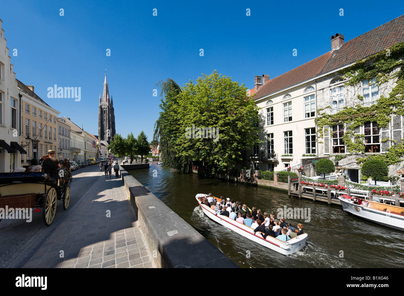Boat trip on a canal in the old town centre with Onze Lieve Vrouwekerk behind,  Bruges, Belgium Stock Photo