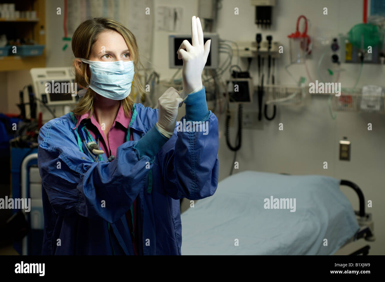 Female nurse in scrubs with face mask putting gloves on