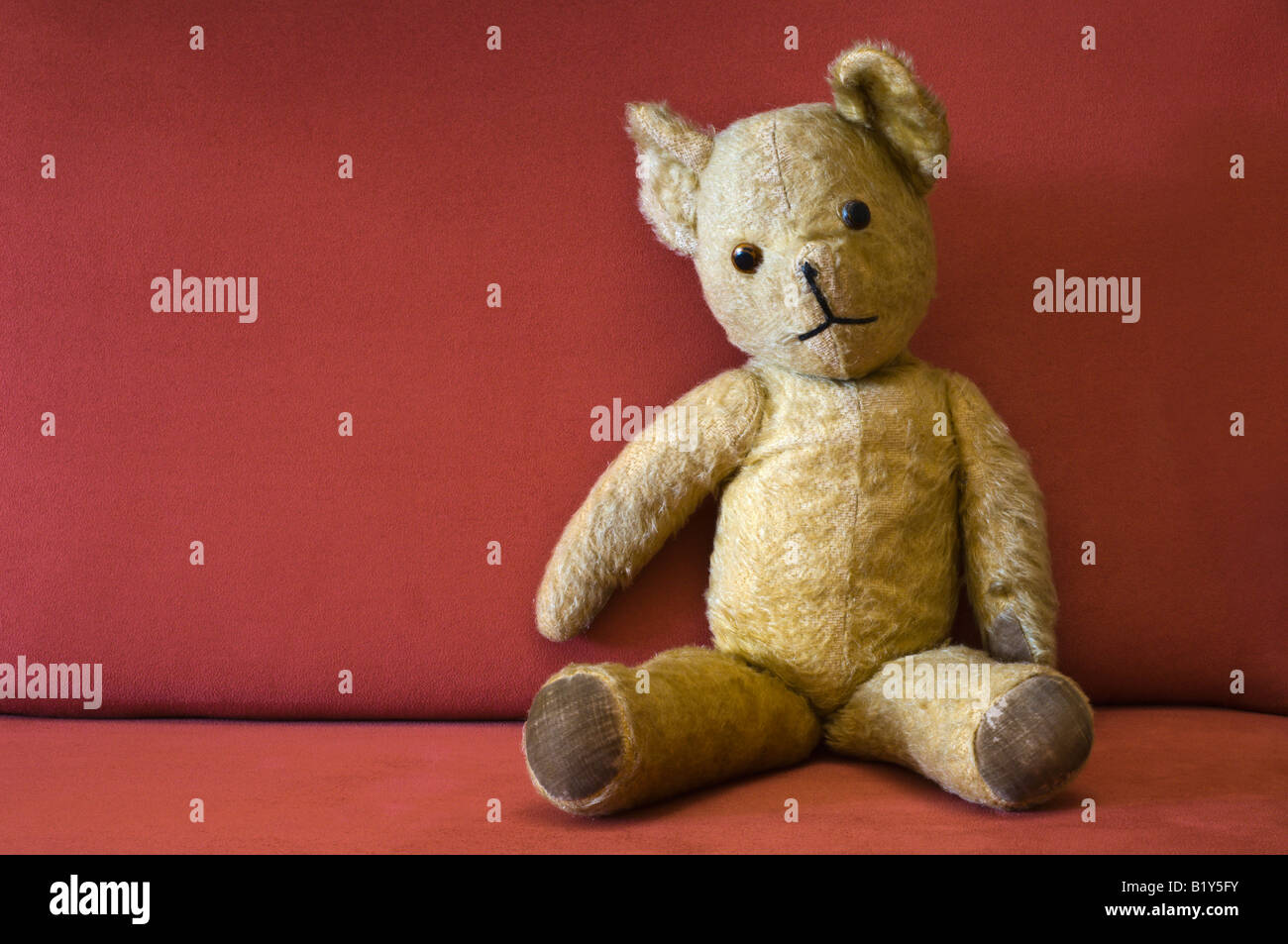 An old fashioned teddy bear seated on a red chair. Stock Photo