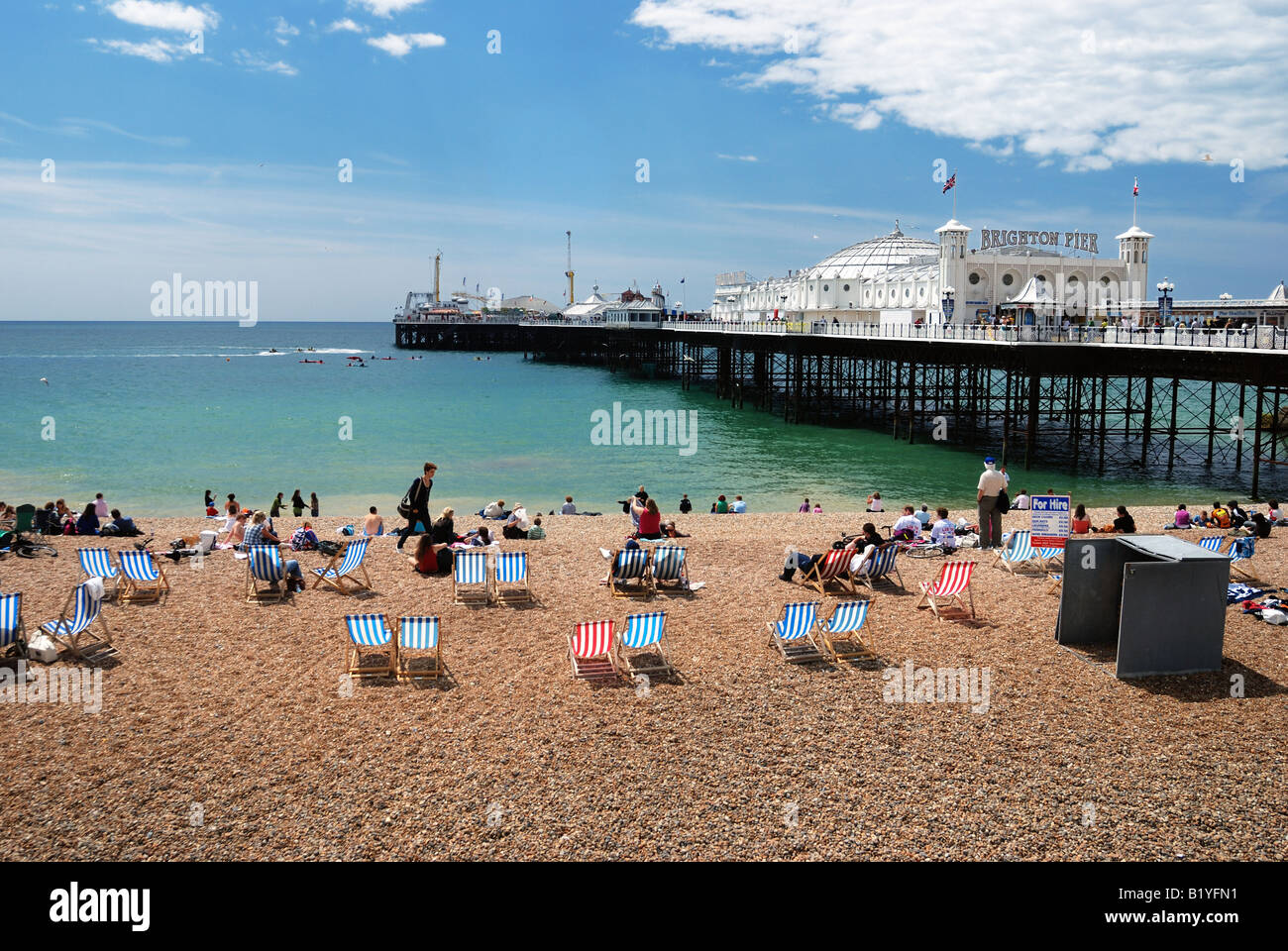 Tourists enjoying the sun on Brighton Beach with Pier in the background Stock Photo