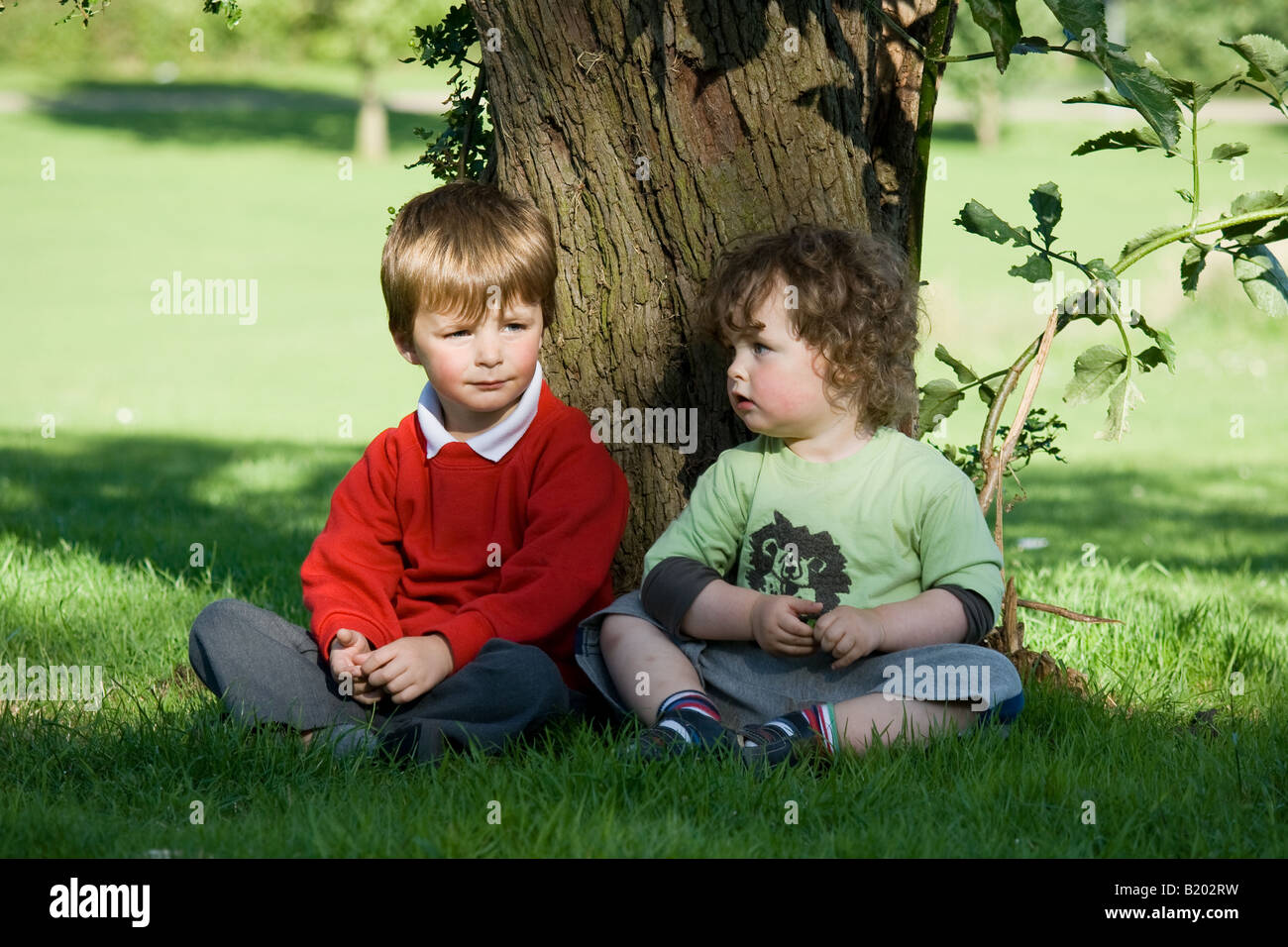 Two Small Boys Sitting Under A Tree In A Park Stock Photo Alamy