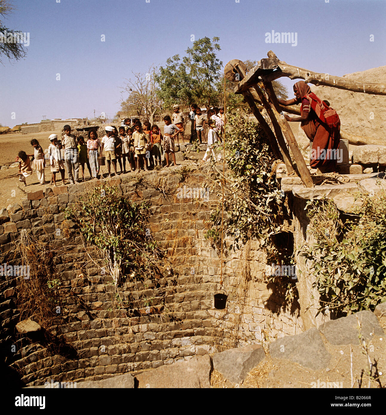 Water from the well, a crowd of children watch the woman lower the bucket.This was at Jamkhed and it was the only well for miles Stock Photo