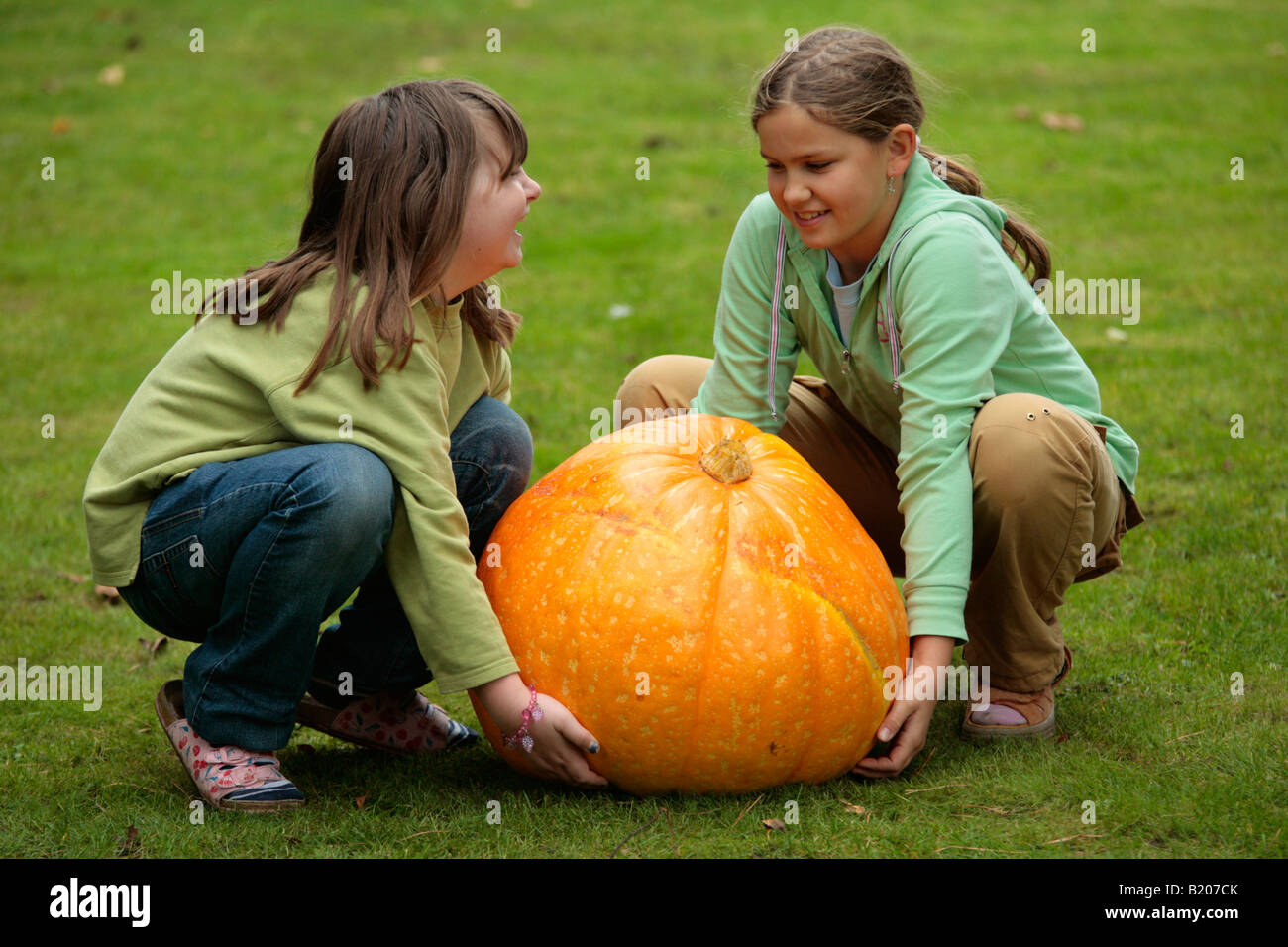 two little girls trying to lift a very big pumpkin Stock Photo - Alamy
