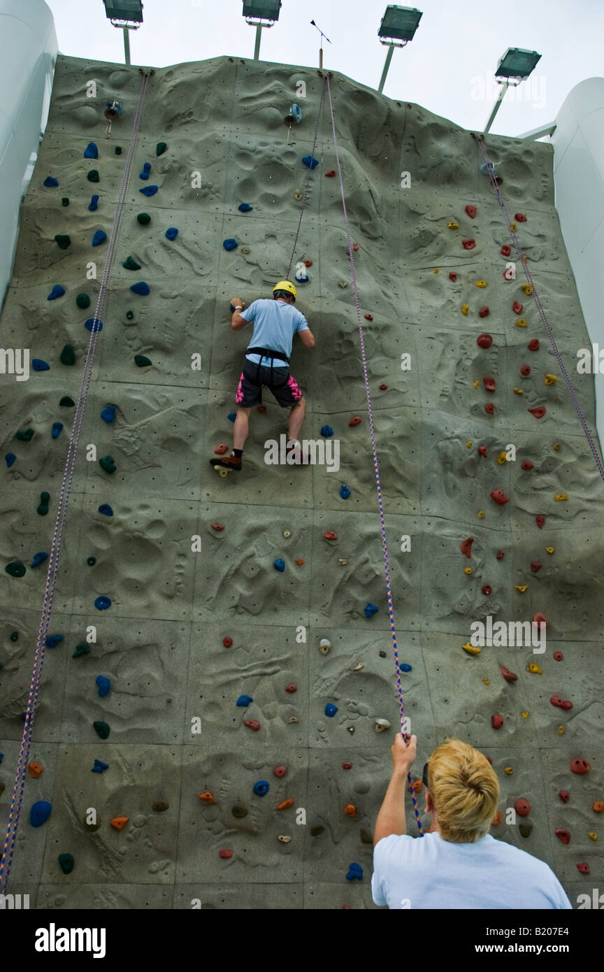 An Instructor holds the Safety Rope of a Climber ascending the Rockclimbing Wall aboard the