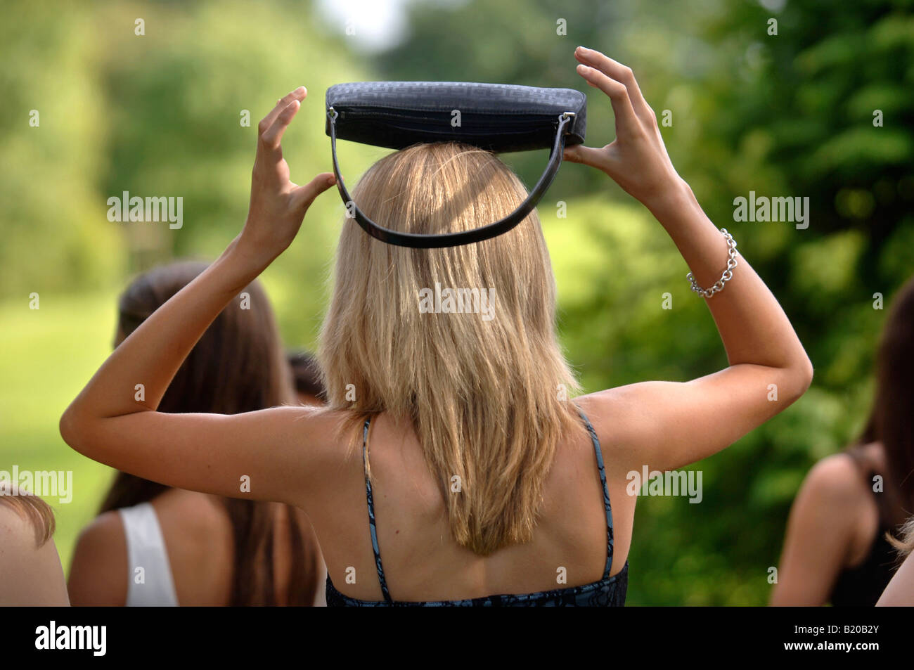 A YOUNG WOMAN IN A PARTY DRESS BALANCES HER HANDBAG ON HER HEAD AT A SUMMER GARDEN FUNCTION UK Stock Photo