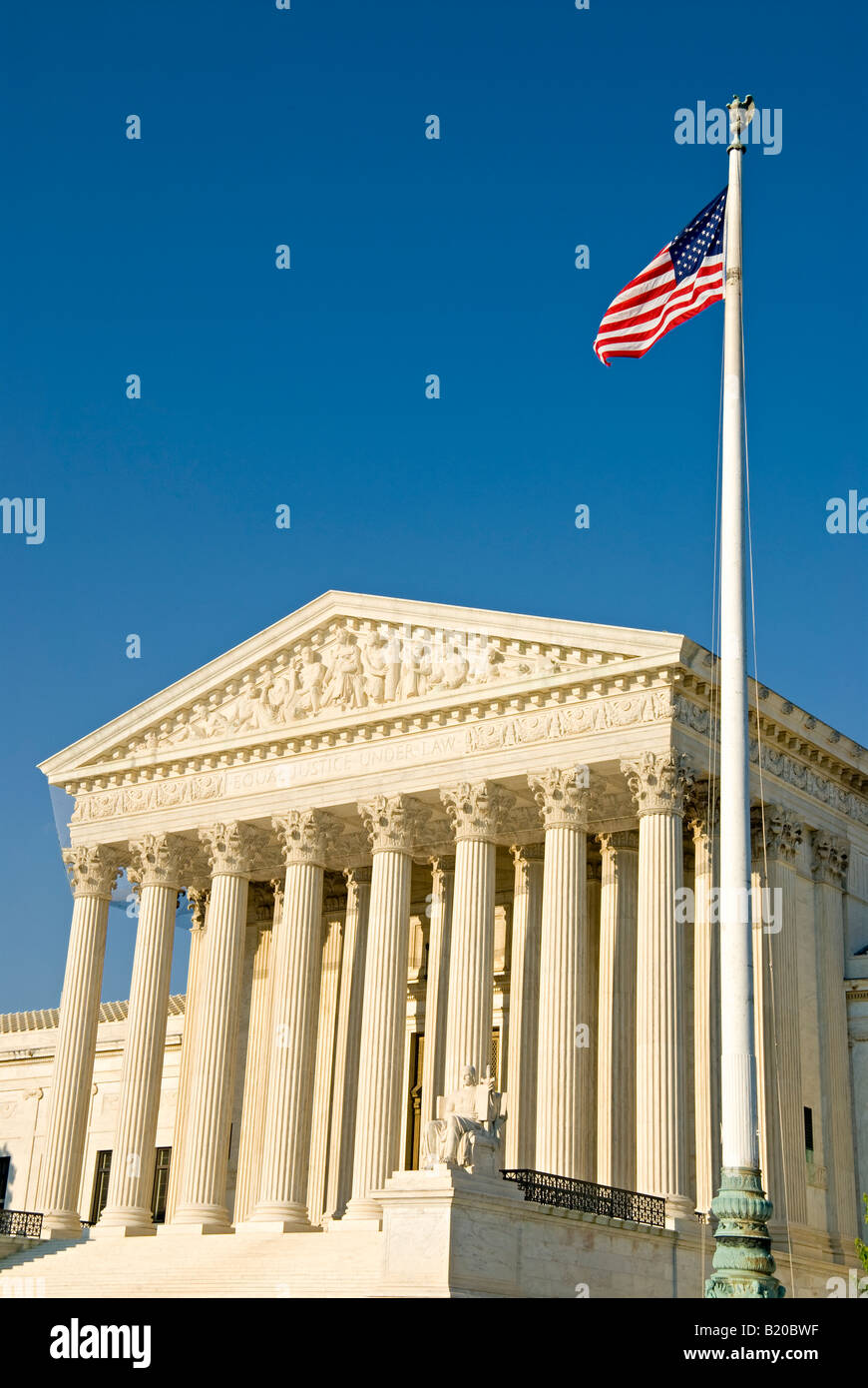 Supreme Court Building American Flag Washington DC // WASHINGTON DC — The United States Supreme Court building stands prominently on Capitol Hill with the American flag visible in the foreground. The neoclassical building, completed in 1935, serves as the seat of the judicial branch of the U.S. government. The Supreme Court consists of nine justices who serve as the final interpreters of federal constitutional law. The building is located at One First Street NE, directly east of the U.S. Capitol building in the nation's capital. Stock Photo