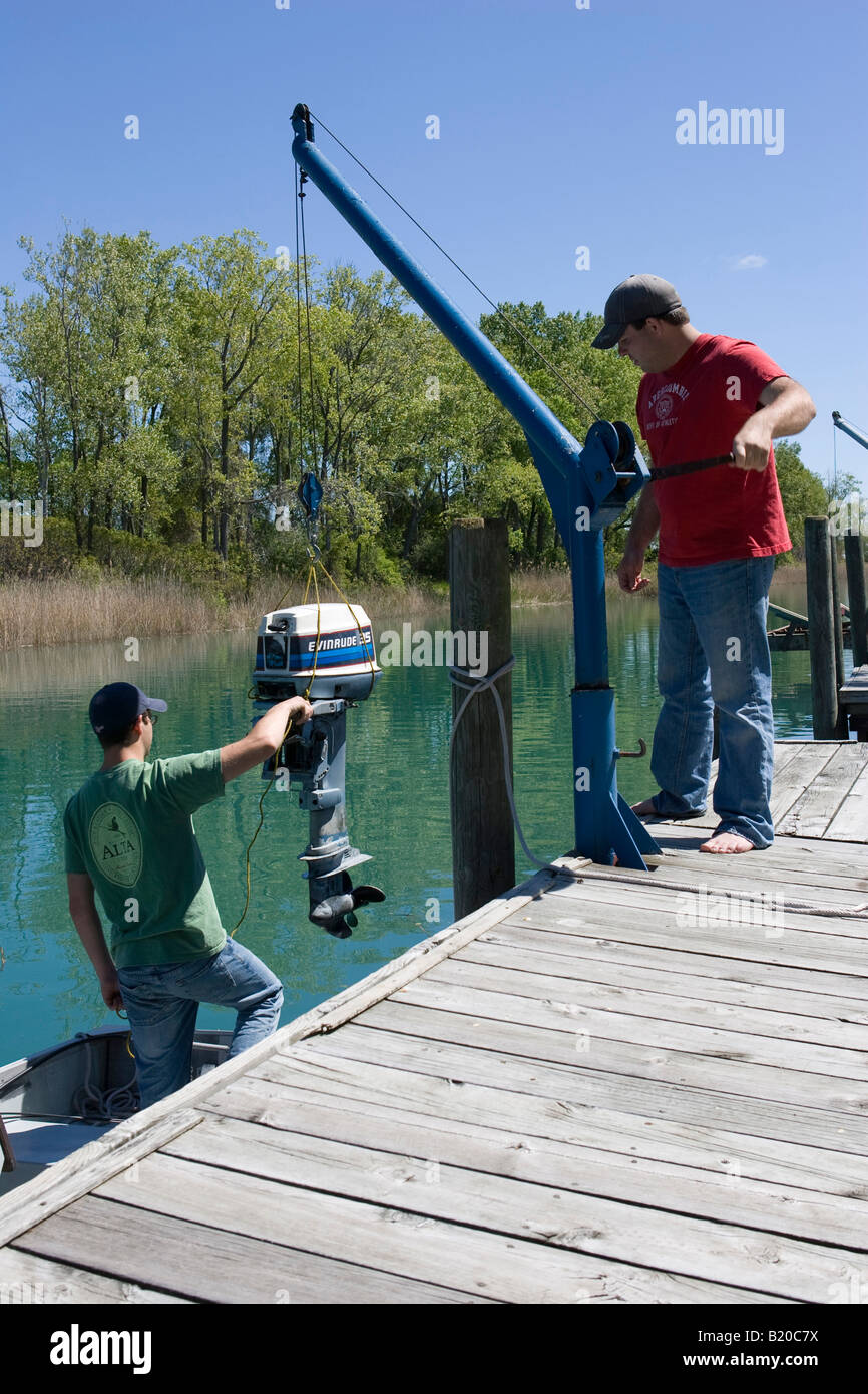 Two men lowering an outboard motor to a boat using a davit hoist Stock