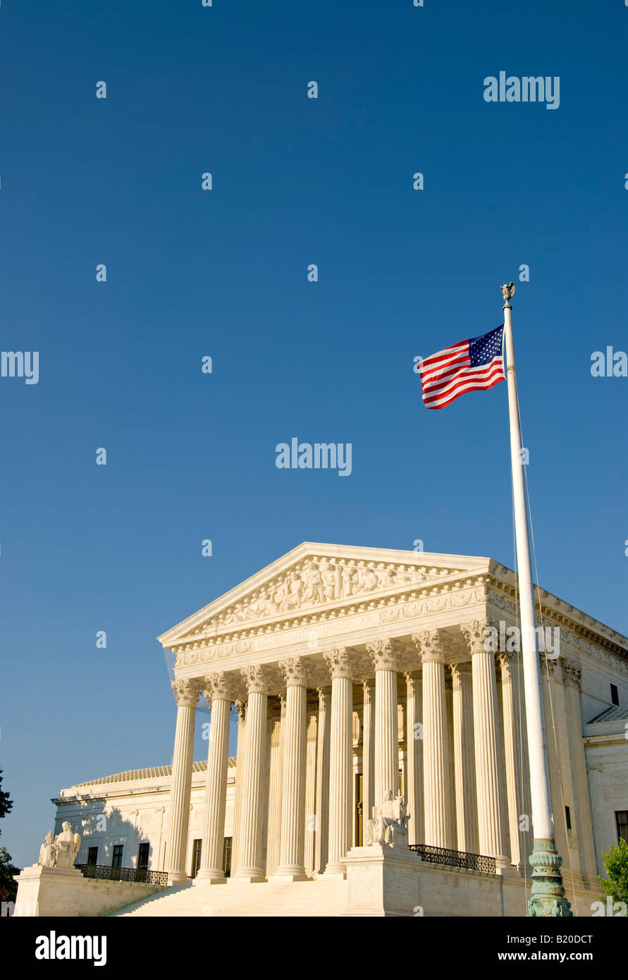 Supreme Court Building American Flag Washington DC // WASHINGTON DC — The United States Supreme Court building stands prominently on Capitol Hill with the American flag visible in the foreground. The neoclassical building, completed in 1935, serves as the seat of the judicial branch of the U.S. government. The Supreme Court consists of nine justices who serve as the final interpreters of federal constitutional law. The building is located at One First Street NE, directly east of the U.S. Capitol building in the nation's capital. Stock Photo