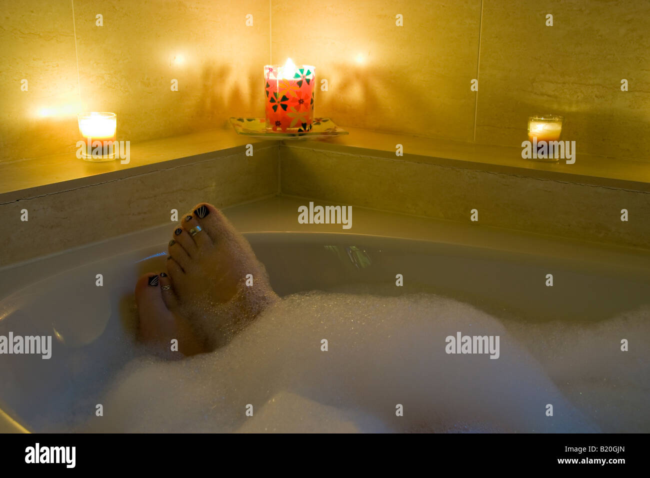 a woman's feet poking through the bubbles in her bath, lit by 3 candles Stock Photo