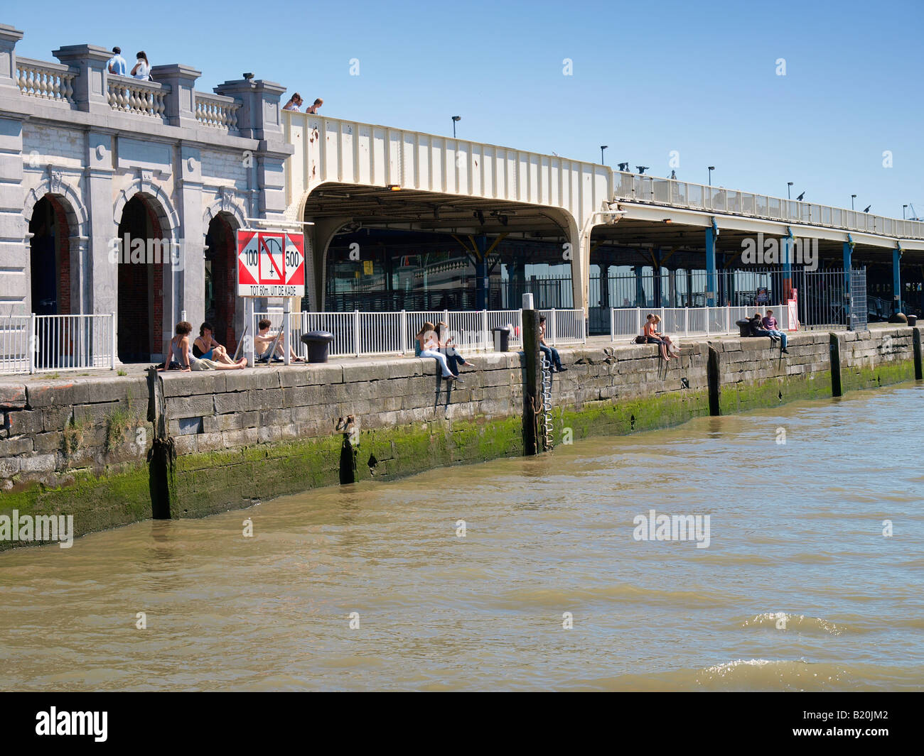 People sitting on the quay bank of the Schelde river in the city center of Antwerp Flanders Belgium Stock Photo