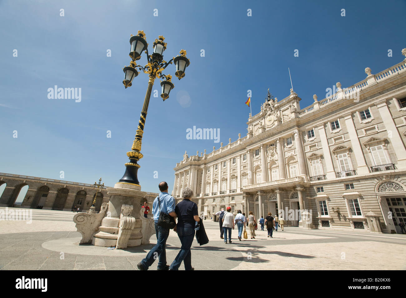 SPAIN Madrid People walking across square outside Royal Palace built by King Philip V in the 18th century wrought iron lampstand Stock Photo