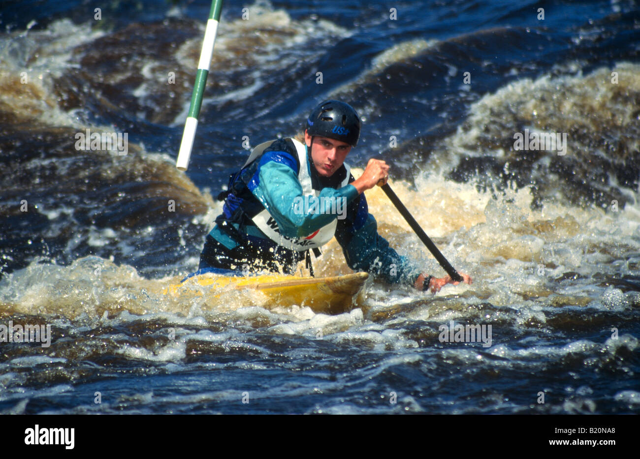 KAYAKING C1 male kayak paddler dig with paddle to maneuver past slalom gate on whitewater race course Stock Photo