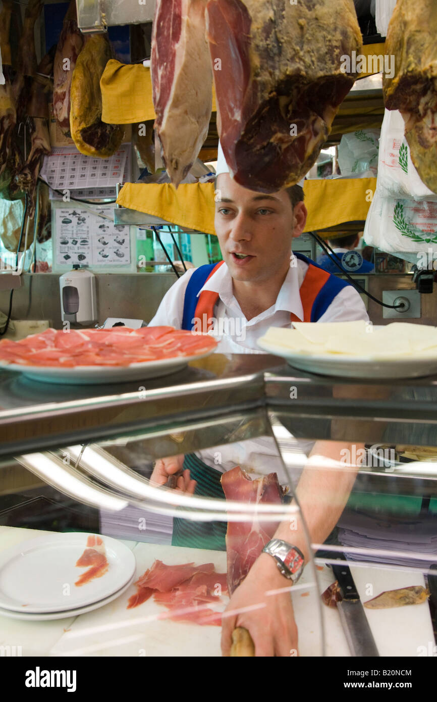SPAIN Madrid Young man slicing ham in Museo de Jamon retail store behind delicatessen counter shanks of meat hanging Stock Photo