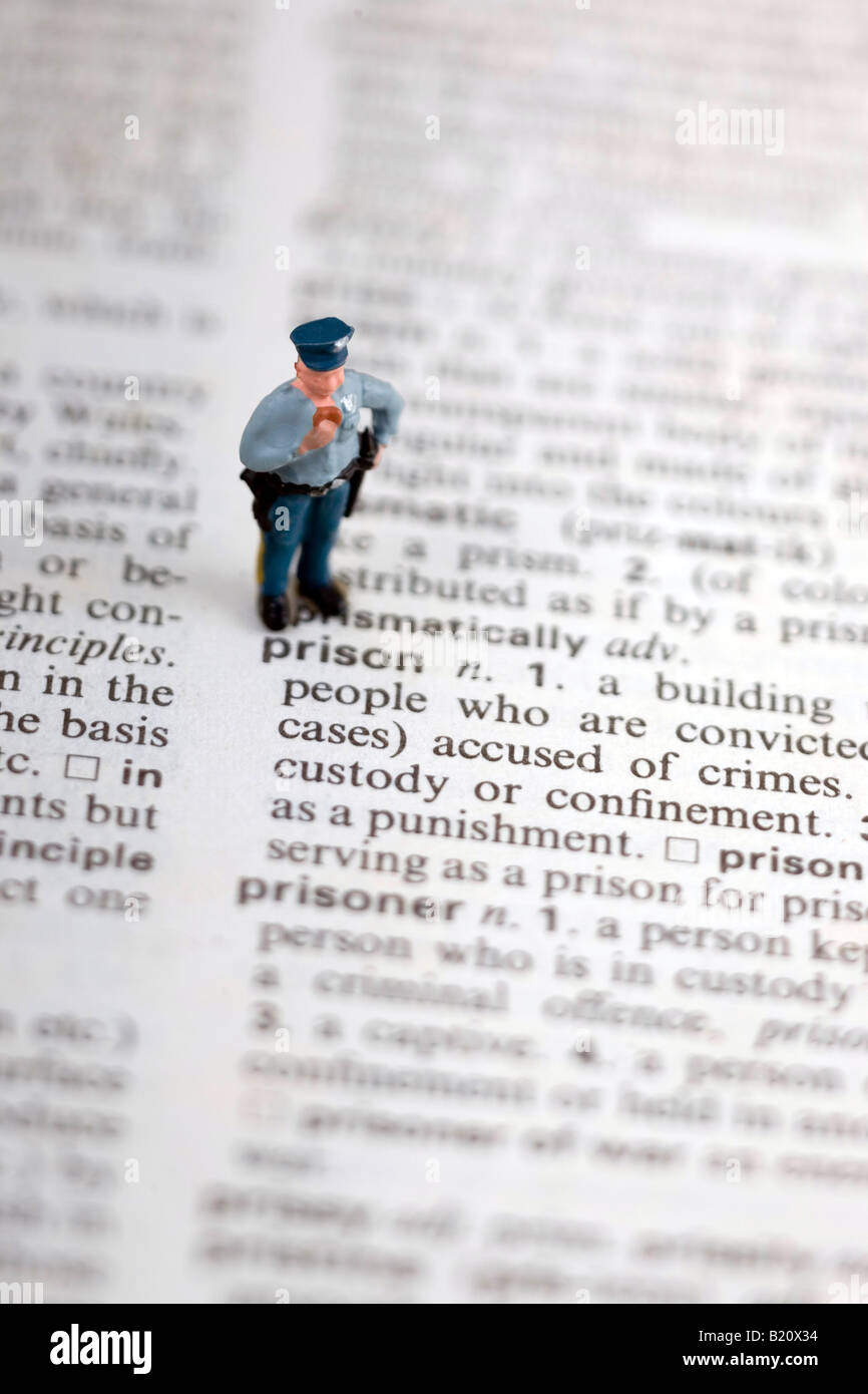 A miniature model of a fat cop eating a donut is standing on a dictionary overlooking the word prison Stock Photo
