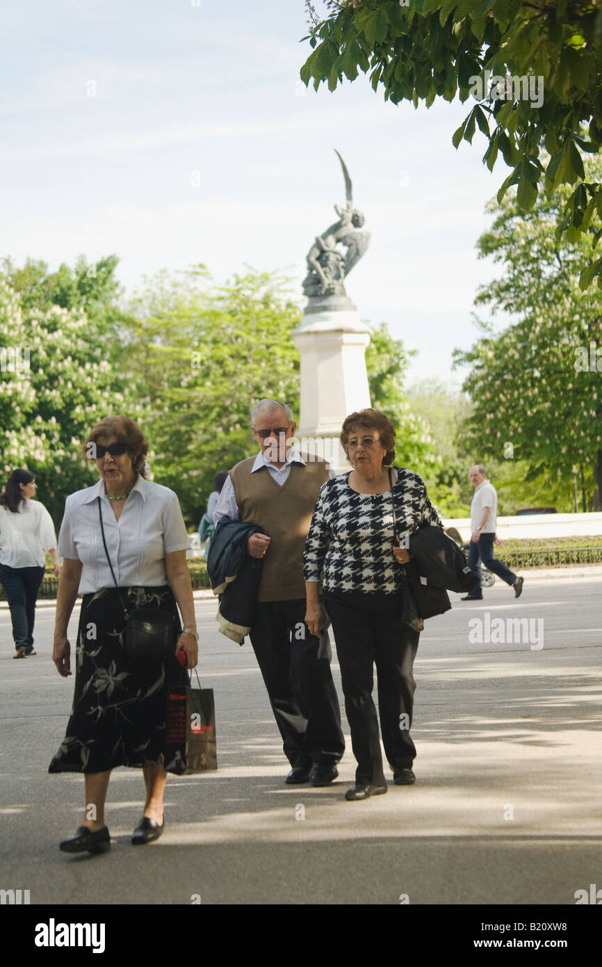 SPAIN Madrid Spanish adults walk on sidewalk through gardens in Retiro Park Parque del Buen Retiro near fountain Stock Photo