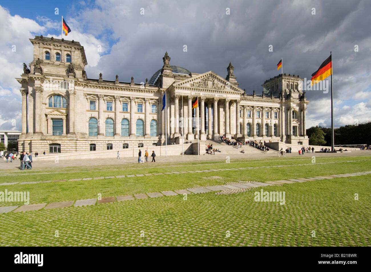 A wide angle view of the Reichstag (German Parliment Building) and tourists on a sunny day with dark clouds behind. Stock Photo
