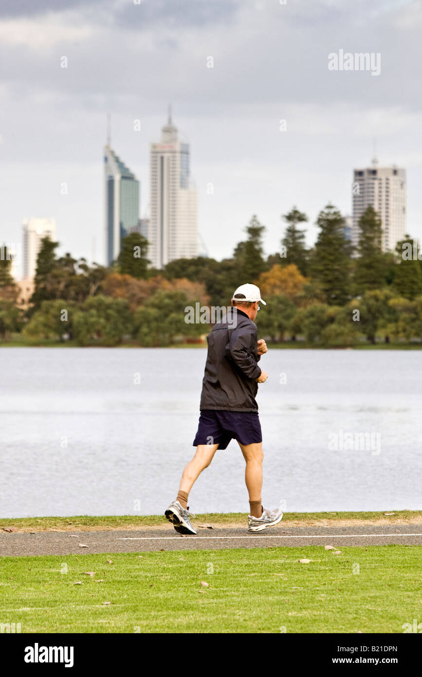 A middle aged man jogging beside a lake with skyscrapers in the distance. Lake Monger, Perth