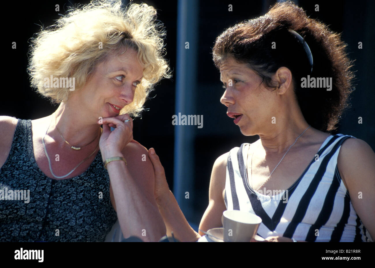 two middle aged women gossiping over coffee on outside terrace Stock Photo