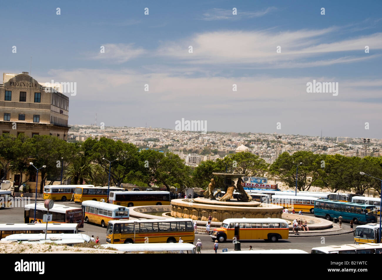 The bus terminal in Valletta is a roundabout at the Triton Fountain.  The classic buses in orange and yellow surround fountain. Stock Photo