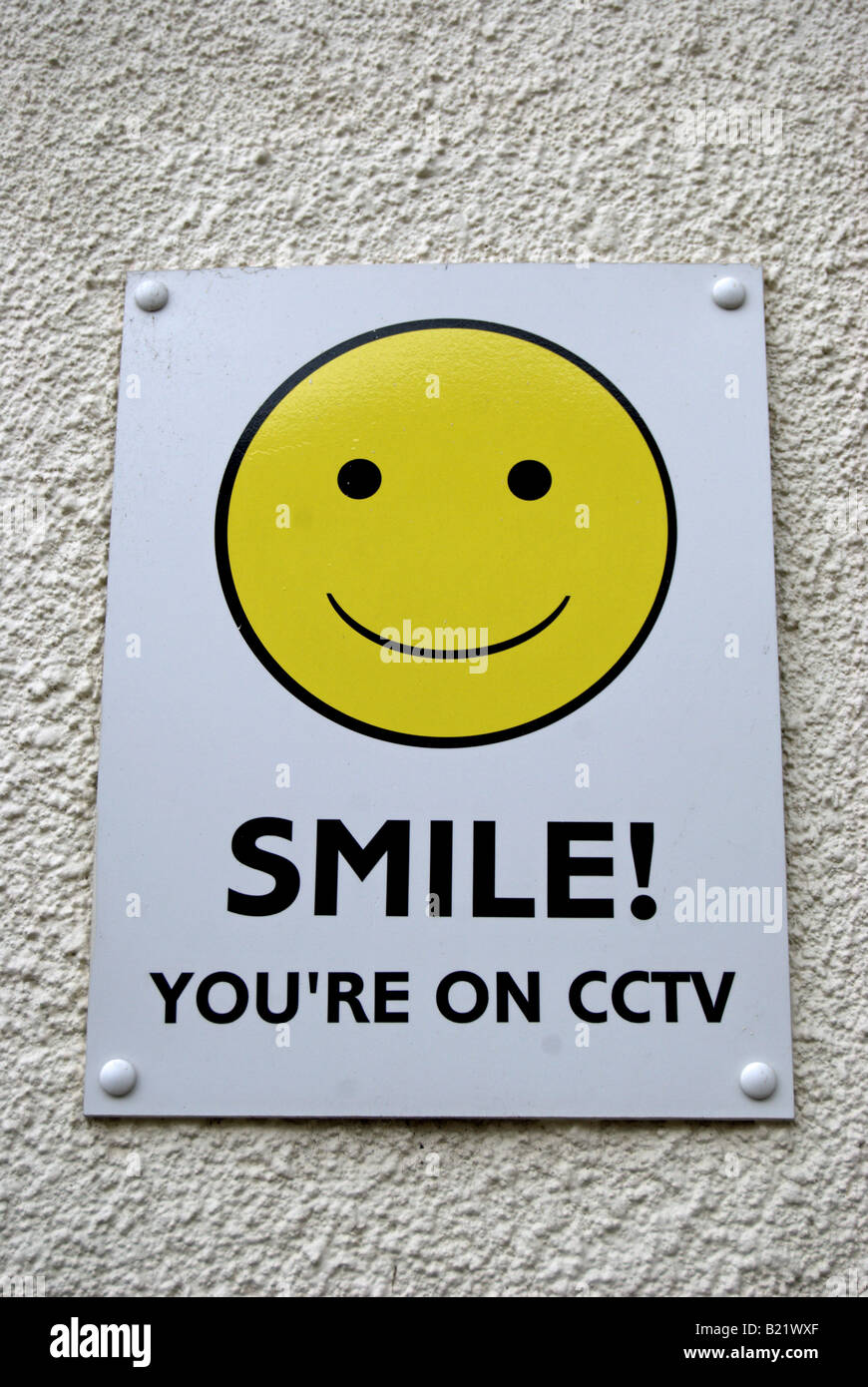 british cctv warning sign with yellow smiley face on white textured wall Stock Photo