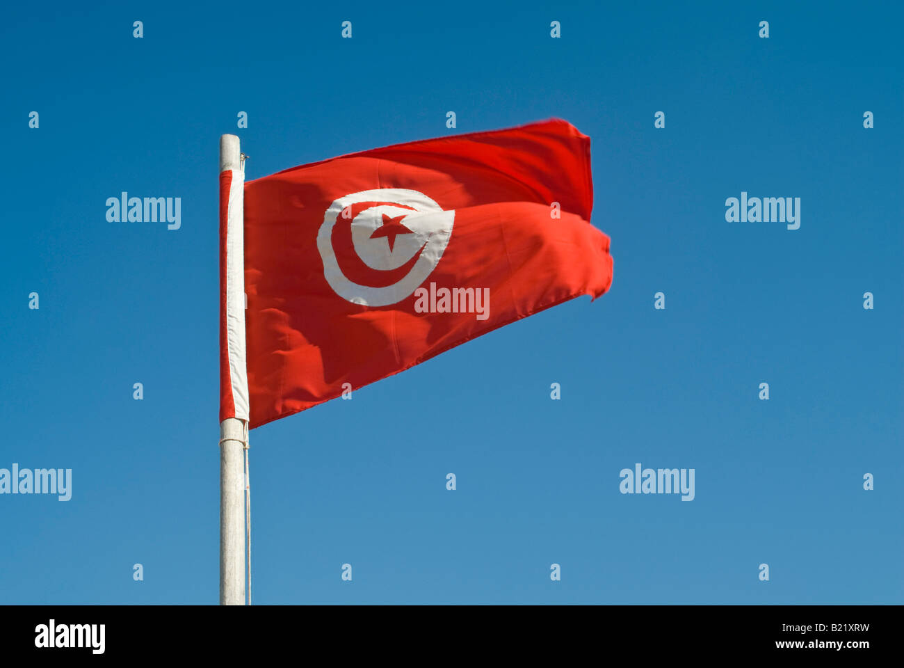 Horizontal close up of the 'post 1999' Tunisian flag with red crescent and star against a blue sky Stock Photo