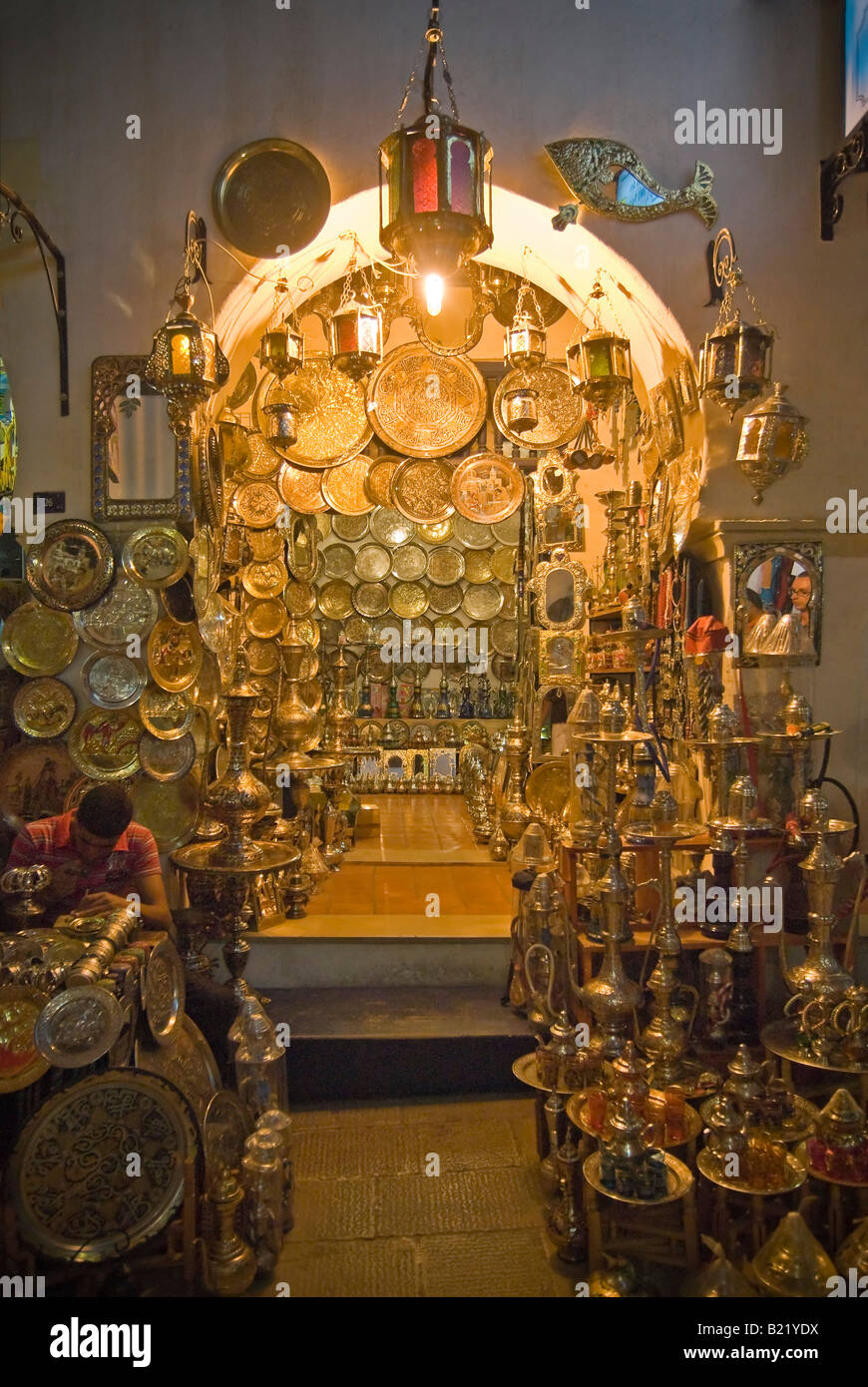 Vertical night time view outside of a traditional Tunisian metalwork shop packed full of brass plates, teapots and lanterns Stock Photo